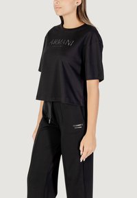 Camiseta negra corta de algodón con mangas cortas y escote redondo, que presenta un brillante logo de "Armani Exchange" en la parte frontal.