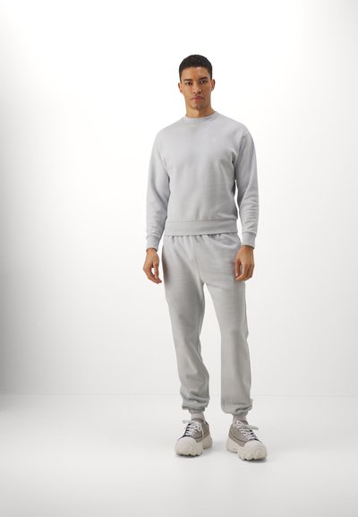 Conjunto de sudadera y pantalones de chándal en una tela suave y lisa. La sudadera presenta un cuello redondo, mientras que los pantalones de chándal tienen una cinturilla elástica y puños.