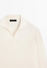 Beige pikétröja med en notch-krage, ribbad textur och en etikett som läser "Massimo Dutti", som visar ett slätt, lättviktsmaterial.
