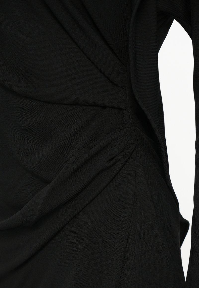 Svart klänning med texturerad, samlad tyg och asymmetrisk drapering samt sömnadsdetaljer på ena sidan. Mjukt, slätt material.