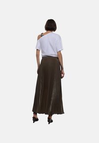 T-shirt bianco oversize con scollatura off-shoulder, abbinato a una lunga gonna plissettata verde oliva. Presenta una texture liscia e una caduta morbida.