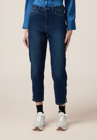 Jeans de mezclilla azul oscuro con un diseño ajustado, que cuentan con un cierre de botón, bolsillos frontales y detalles decorativos de encaje en el tobillo.