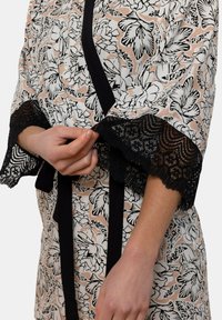 Kimono à motifs floraux avec des manches et une bordure en dentelle noire. Présente une base rose et blanche avec des accents noirs. Se noue à la taille pour la fermeture.