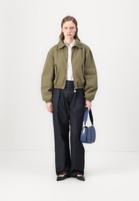 Giacca bomber croppata verde oliva, camicia bianca con bottoni, pantaloni in denim scuri a gamba larga e borsa blu con tracolla corta. Scarpe flat nere.