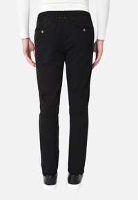 Pantaloni in cotone neri con vestibilità slim, dotati di due tasche posteriori con bottoni tondi e una vita con passanti per cintura e inserti elastici.