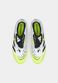 Pantofi sport albi și negri cu un toc texturat, accente galbene strălucitoare, o formă aerodinamică și un branding proeminent pe limbă.