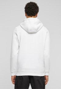 Hoodie blanc avec capuche à cordon, en tissu doux, avec des poignets et un ourlet côtelés. Présente un design à coupe droite sans graphiques visibles.