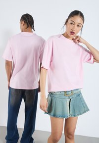 Rosa bomull T-skjorte med avslappet passform og senkede skuldre, sendt med en denim plisserte skjørt med belte. Bakvinkel av forskjellige modeller.