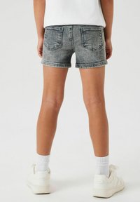 Pantalones cortos de mezclilla en un lavado negro desgastado, con dobladillo enrollado y dos bolsillos traseros, combinados con zapatos blancos y calcetines cortos.