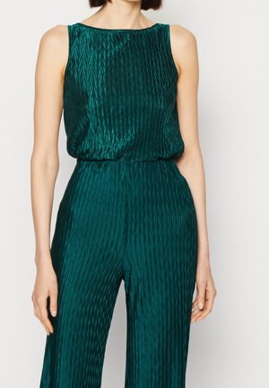 Combinaison sans manches vert émeraude avec un motif zigzag vertical texturé et un haut blouson rentré dans un pantalon large.