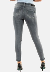 Jeans gris skinny avec une texture lisse, dotés de poches arrière avec des coutures incurvées et une taille noire. Portés avec des talons noirs.