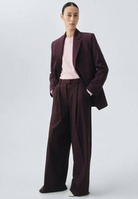 Maroon tailored blazer over a light pink sweater, paired with wide-leg maroon trousers. Fabric appears smooth and structured.