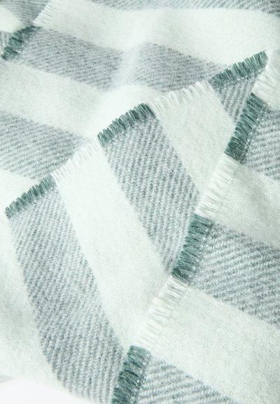Μαλακή μάλλινη κουβέρτα με μεγάλο καρό σχέδιο σε ανοιχτό γκρι και λευκό χρώμα και κοντές φουντίτσες στα άκρα.