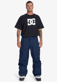Marina skidbyxor tillverkade av hållbart tyg, med en avslappnad passform och flera fickor. Tillsammans med en svart DC-logotyp t-shirt.