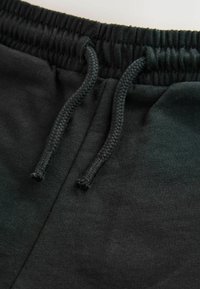 Mustad puuvillased dressipüksid, millel on elastne vöökoht paelaga. Kangastekstuuri ja õmbluste detailide suletud vaade.