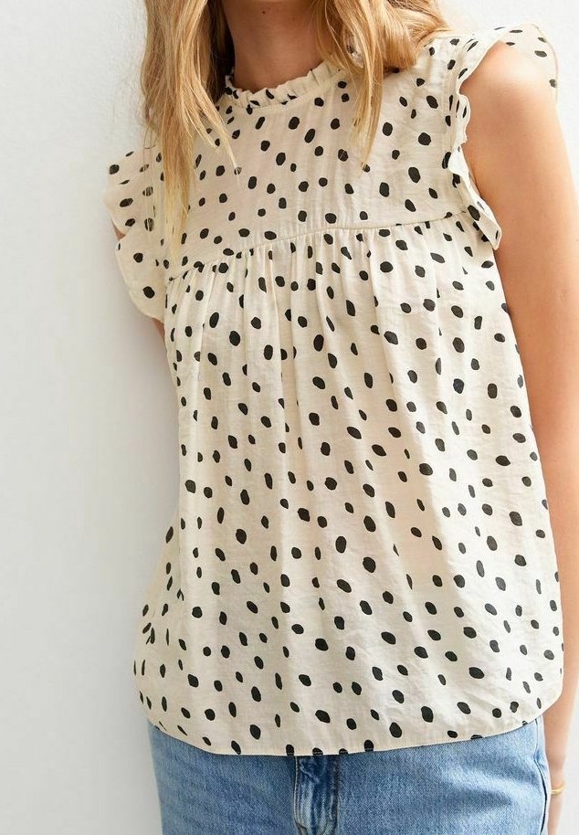 Top beige chiaro con pois neri, maniche corte a volant e scollo arricciato. Tessuto morbido e leggero con vestibilità comoda.