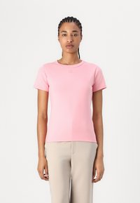 T-shirt rose clair à manches courtes avec un col rond et un logo discret sur la poitrine, fabriqué à partir de tissu doux et extensible.
