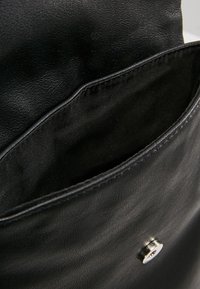 Intérieur d'un sac en cuir noir montrant une texture lisse, avec une fermeture à bouton pression argenté et un design de poche profonde. Coutures minimales visibles.