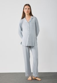 Ljusblått pyjamasset med lång ärm gjort av mjukt tyg; har kontrasterande vit pipning, en ficka på toppen och raka byxor.