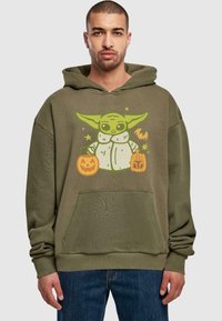 Olivgrön hoodie med en tecknad karaktär med stora öron som håller två pumpor. Materialet är mjukt och med en framficka.