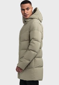 Olivgrüne Daunenjacke mit Kapuze, ausgestattet mit gestepptem Futter, einem Reißverschluss vorne und einem Logo auf der Brust. Das Design ist lang und gerade geschnitten.