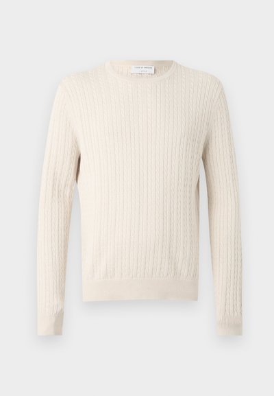 Πουλόβερ σε κρεμ απόχρωση με πλεκτό σχέδιο, μακριά μανίκια και στρογγυλή λαιμόκοψη, που εμφανίζεται σε απλό, ανοιχτό φόντο.