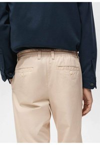 Béžové kalhoty s elastickým pasem a dvěma zadními kapsami na knoflíky. Kombinované s tmavě modrou košilí s dlouhým rukávem. Hladká textura.