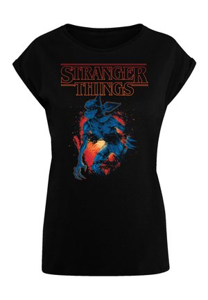 Black t-shirt featuring a blue creature graphic from "Stranger Things." Text is in bold orange above the design, with a textured look.