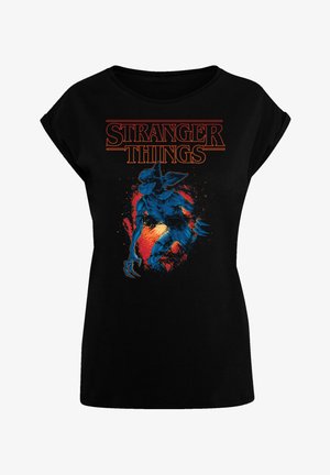T-shirt noir avec un graphique d'une créature bleue de "Stranger Things". Le texte est en orange gras au-dessus du design, avec un aspect texturé.