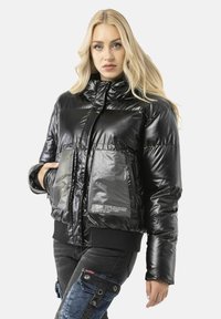 Schwarze Steppjacke mit glänzendem Finish, verfügt über zwei transparente Taschen, hohen Kragen sowie gerippte Bündchen und Saum. Textdetails auf der Tasche.