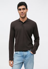 Polo marrone a maniche lunghe con una texture a coste e una patta con tre bottoni. Abbinata a jeans di denim azzurro chiaro.