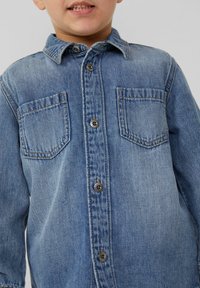 Lichtblauw denim shirt met een kraag, twee borstzakken en een sluiting met knopen aan de voorkant. Het heeft zichtbare stiksels en een zachte textuur.