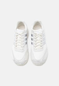 Bijele tenisice s tri srebrne pruge, gornji dio od teksturiranog platna, okrugli vrh i dizajn na vezice. Naglašeni potplat s suptilnim detaljima.