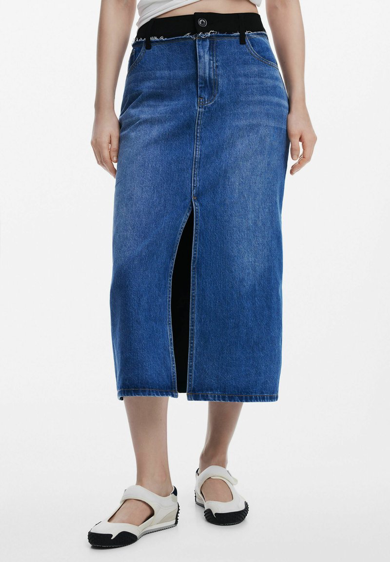 Denim midi kjol i blått med sprund fram och fransad nederkant. Har ett svart midjeband med en knapp och sidofickor. Kombineras med vita skor.