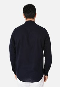 Camicia a maniche lunghe blu navy realizzata in tessuto leggero, con colletto classico, polsini abbottonati e orlo curvo. Senza motivi o dettagli.