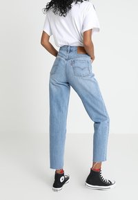 Ljusblå högmidjade jeans med avslappnad passform, fransade avslut och en läderpatch på baksidan. I kombination med svarta högstövlar.