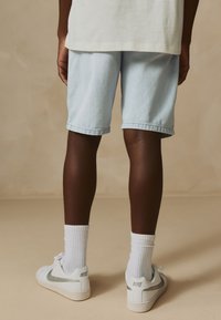 Light blue denim shorts with rolled hems, paired with white socks and white shoes featuring a silver Nike swoosh, view from the back.
