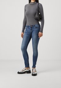 Camiseta de manga larga de canalé gris combinada con jeans ajustados azules y zapatos de plataforma plateados brillantes con correas. También se puede ver un bolso negro de hombro.