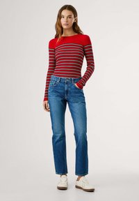 Top de manga larga acanalado a rayas rojas y negras con diseño ajustado, combinado con jeans de pierna recta azules y zapatillas blancas.
