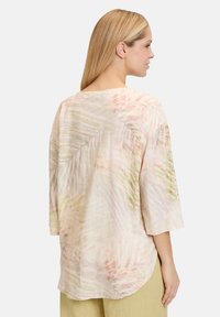 Canotta leggera beige con maniche a tre quarti, caratterizzata da un sottile motivo di foglie di palma in morbidi colori pastello e un orlo arrotondato.