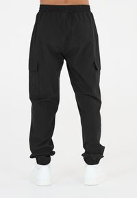Svarta cargo-byxor med elastisk midja, sidofickor och avskurna fållar. Tillverkade av ett slätt, lätt material. Bärs med vita sneakers.