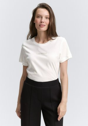 T-shirt en coton blanc avec un col rond et des manches courtes. Présente le logo "TOM TAILOR" en gris clair. Porté avec un pantalon noir ajusté.