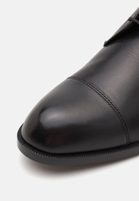 Zapato de cuero negro con punta redondeada, textura suave y costuras detalladas a lo largo de la costura, con un borde de suela ribeteado.