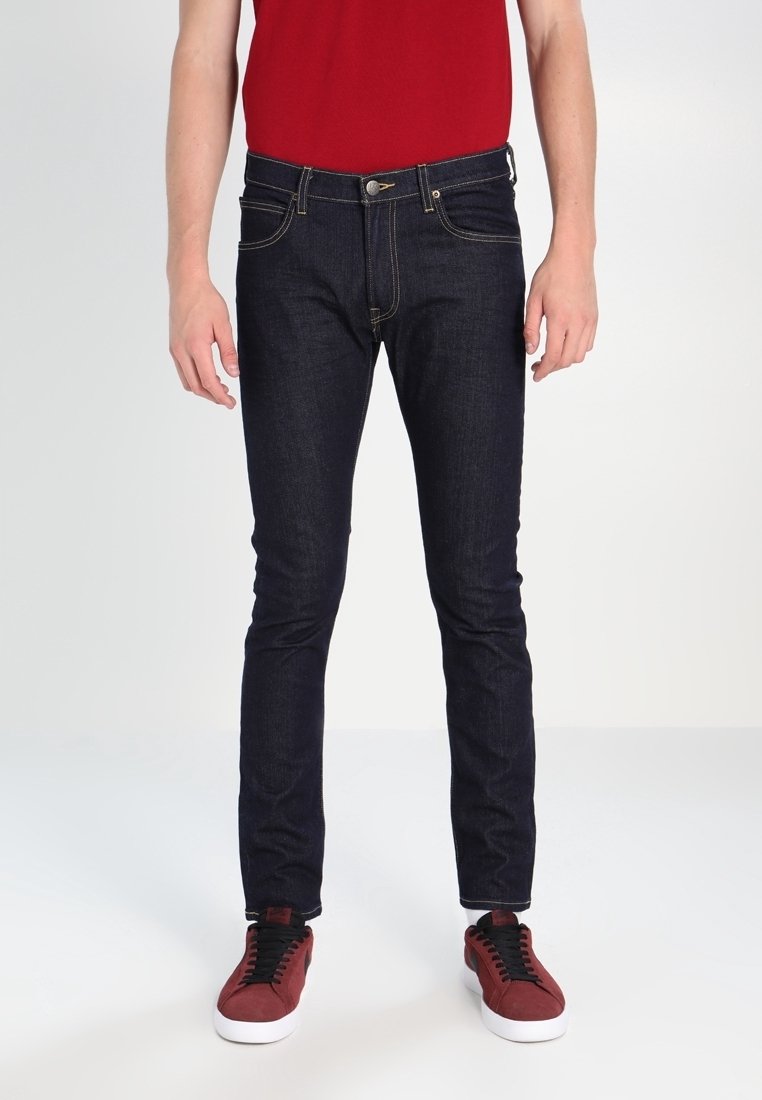 Tmavě modré džínové kalhoty slim fit, s žlutým prošíváním, pěti kapsami a zipem. Doplňují je červené tenisky.