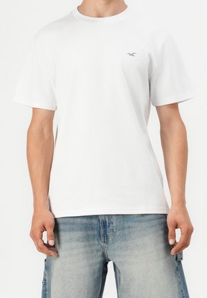 T-shirt en coton blanc avec un col rond et des manches courtes. Présente un petit logo gris clair sur le côté gauche de la poitrine.