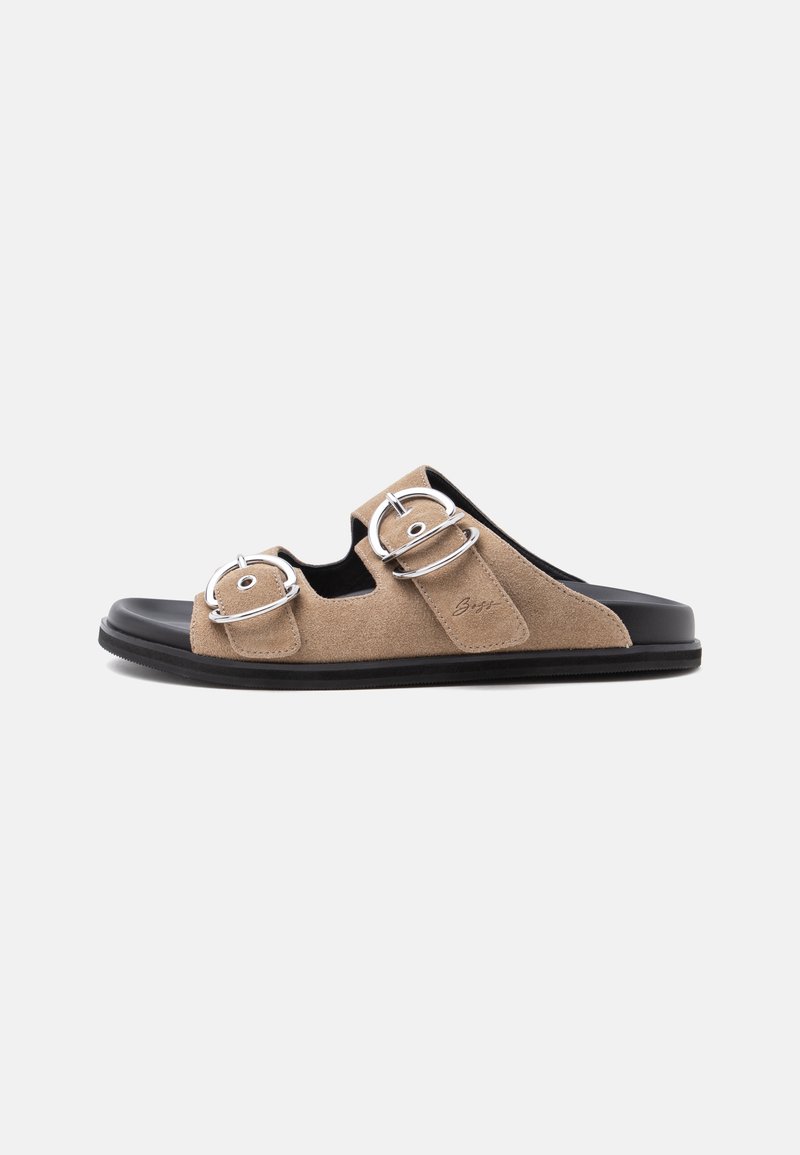 Sandale à enfiler en daim beige pour homme avec deux boucles argentées et semelle noire, vue de profil sur fond uni.