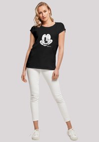 Juodas trumpomis rankovėmis marškinėliai su dideliu baltu Mickey Mouse veido atvaizdu. Sukombinuota su baltais siauriais džinsais ir baltais sportbačiais.