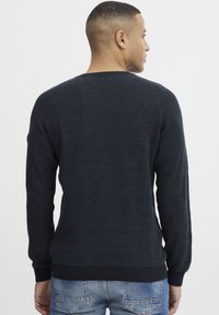 Mørk marineblå strikkegenser med et teksturert design, ribbede mansjetter og hem, med rund hals og en tettsittende silhuett.