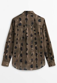 Pitkähihaista paitaa vaaleanruskeana, jossa on musta abstrakti pistekuvio; varustettu kauluksella ja pyöristetyllä helmalla; pehmeää, teksturoitua kangasta.