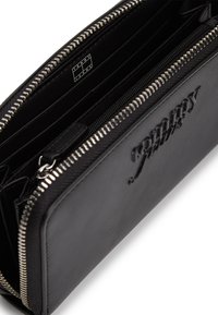 Μαύρο δερμάτινο πορτοφόλι με πολλαπλές θήκες, ασημένιο μεταλλικό εξάρτημα και ανάγλυφο λογότυπο. Διαθέτει φερμουάρ και υφή εσωτερικά.